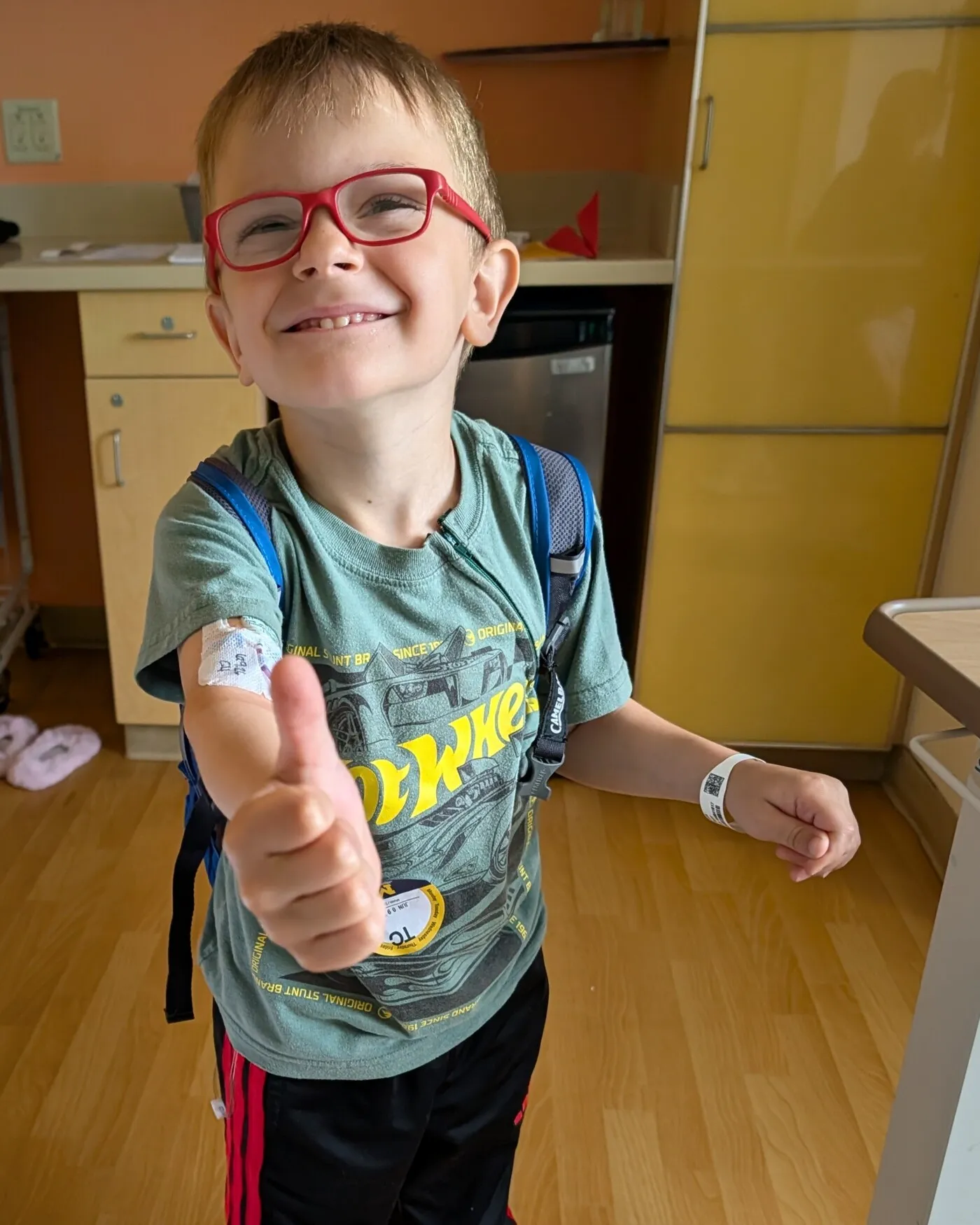 A smiling young boy in a hospital room giving a thumbs up